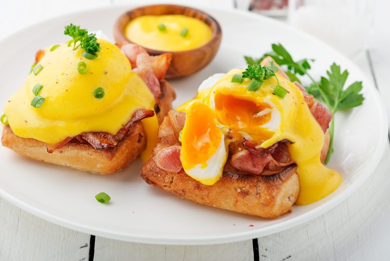 Eggs benedict with bacon on white wooden background .